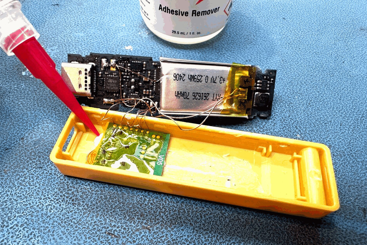 Opened yellow Ledger Nano X with an added green implant board, fine wires and a smaller battery